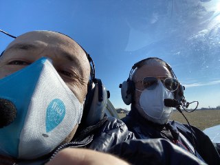 Due uomini con mascherina e cuffie all'interno della cabina di un piccolo aereo