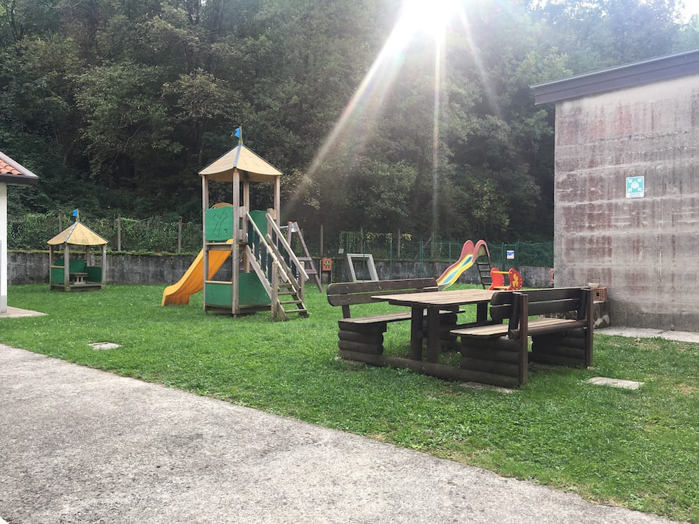 Area giochi con scivolo e casetta in legno, tavolo da picnic su un prato
