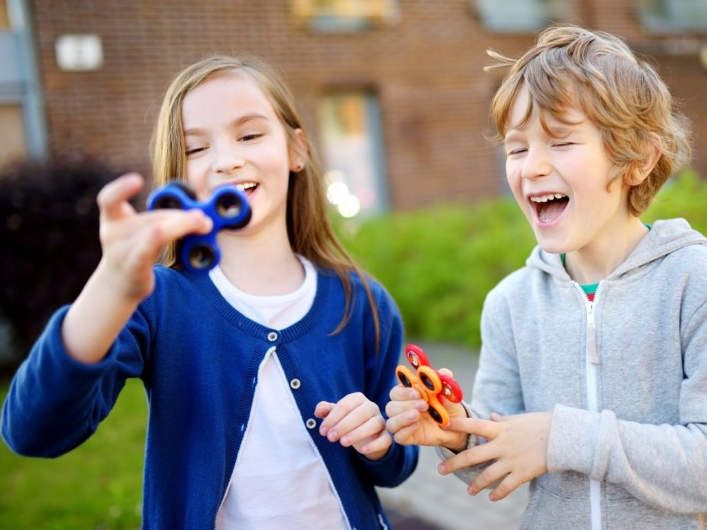 Due bambini sorridenti che giocano con degli spinner colorati all'aperto