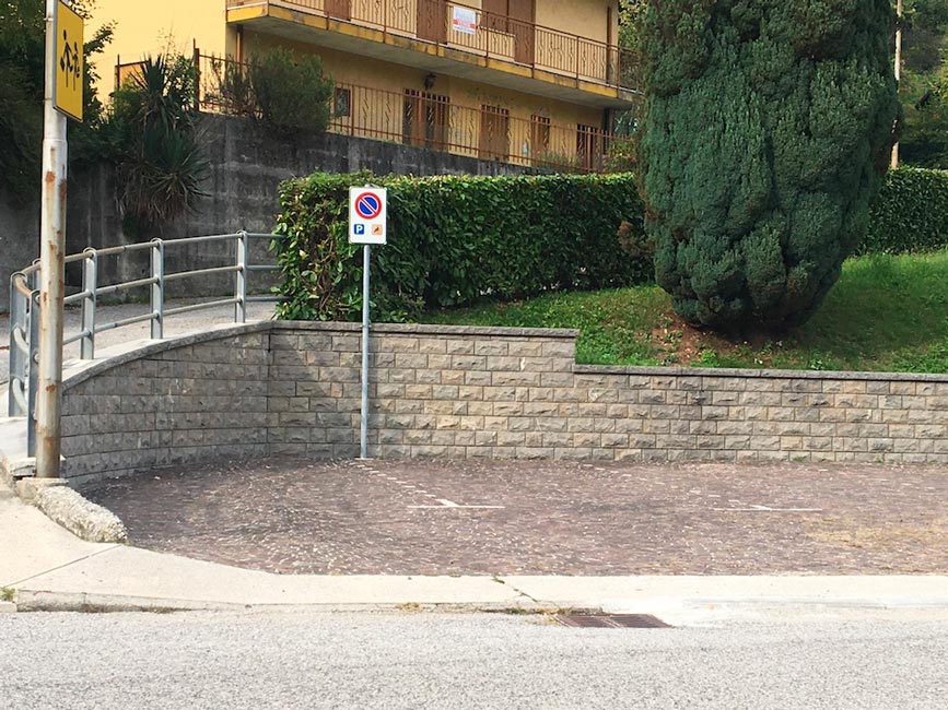 Area di sosta pavimentata con cartello di parcheggio riservato e una rampa con corrimano