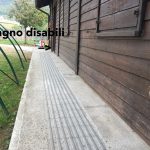 Rampa pavimentata lungo una parete in legno, con cartello che indica il bagno per persone con disabilità